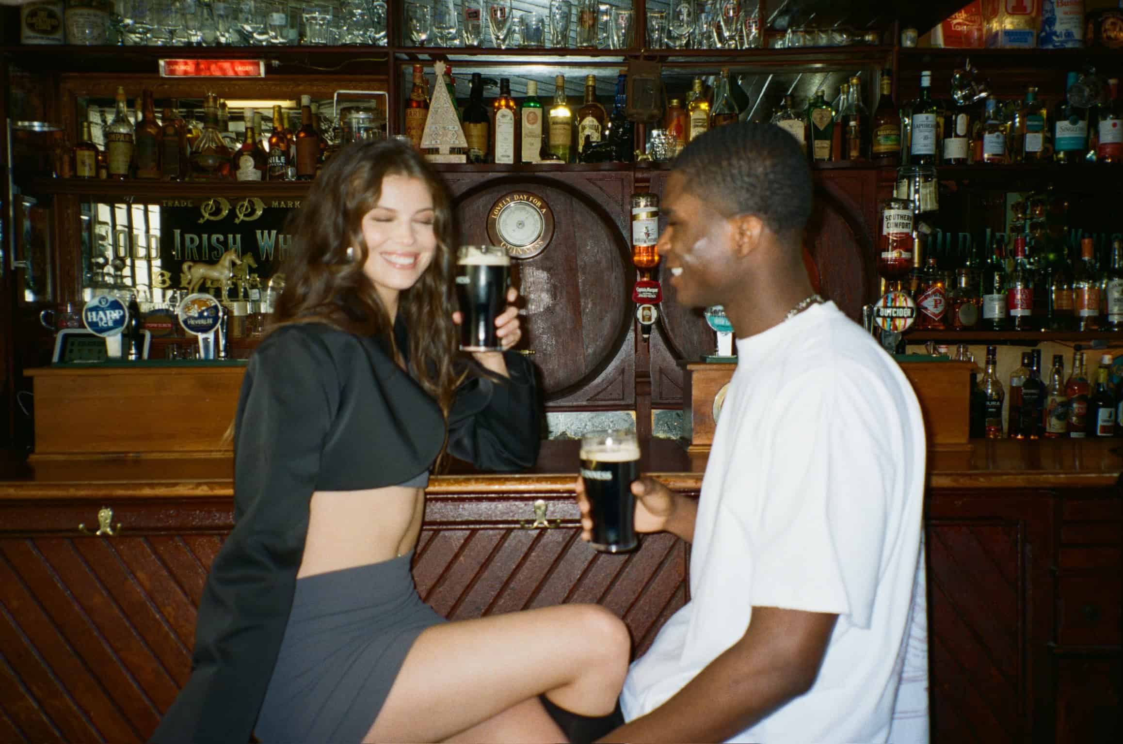 Campaign models Emma and Patrick on 35mm film at the bar with pints of Guinness beaming at the camera, slightly out of focus.