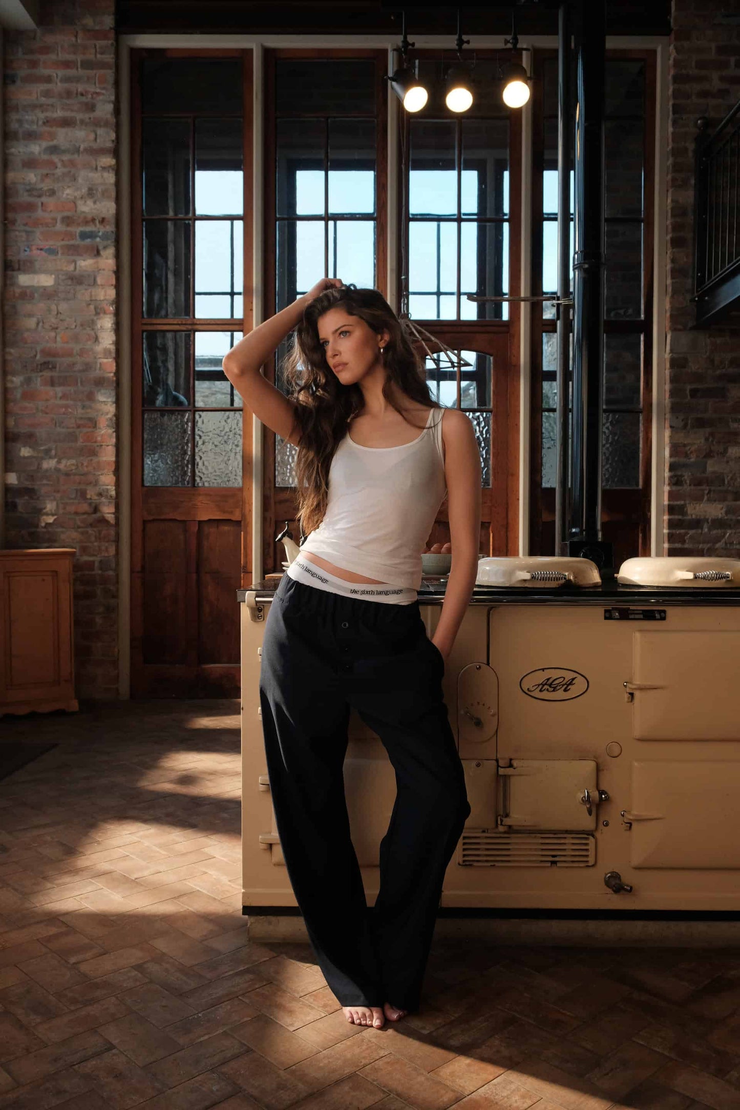 Female model emma posed casually in a rustic kitchen infront of the stove and aga wearing the navy blue apartment pants and briefs by The Sixth Language in their debut collection "the Intro Collection"
