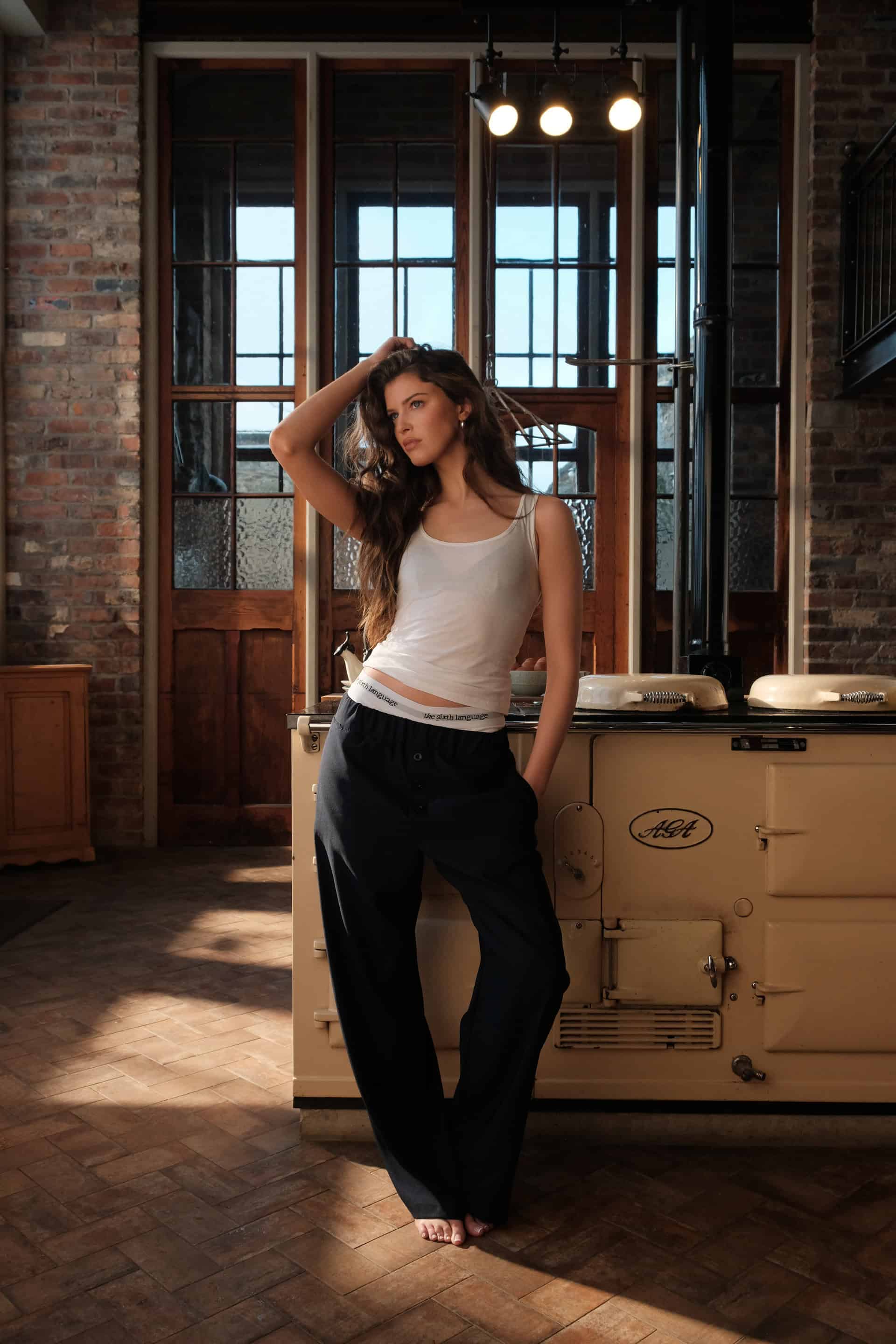 Female model emma posed casually in a rustic kitchen infront of the stove and aga wearing the navy blue apartment pants and briefs by The Sixth Language in their debut collection "the Intro Collection"
