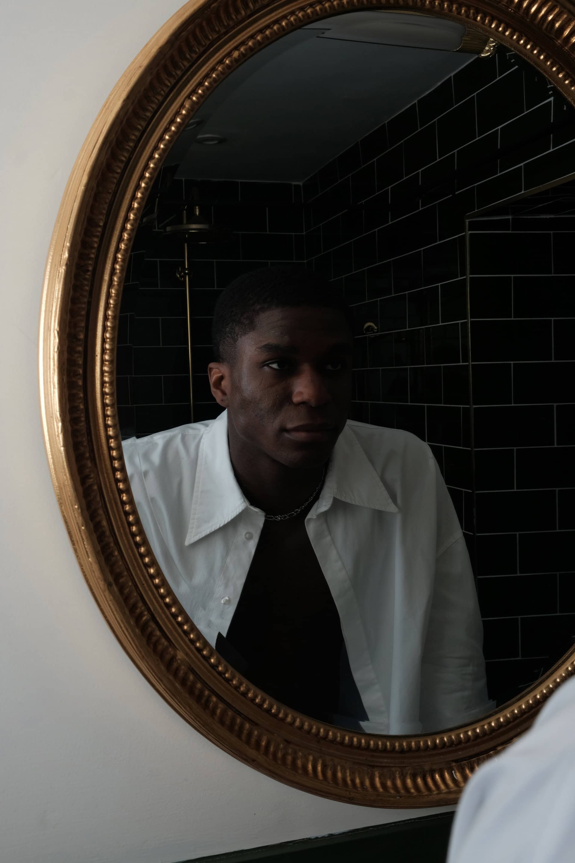 Male model Patrick looking at himself in a gold trimmed mirror wearing the Seasons shirt open casually. 