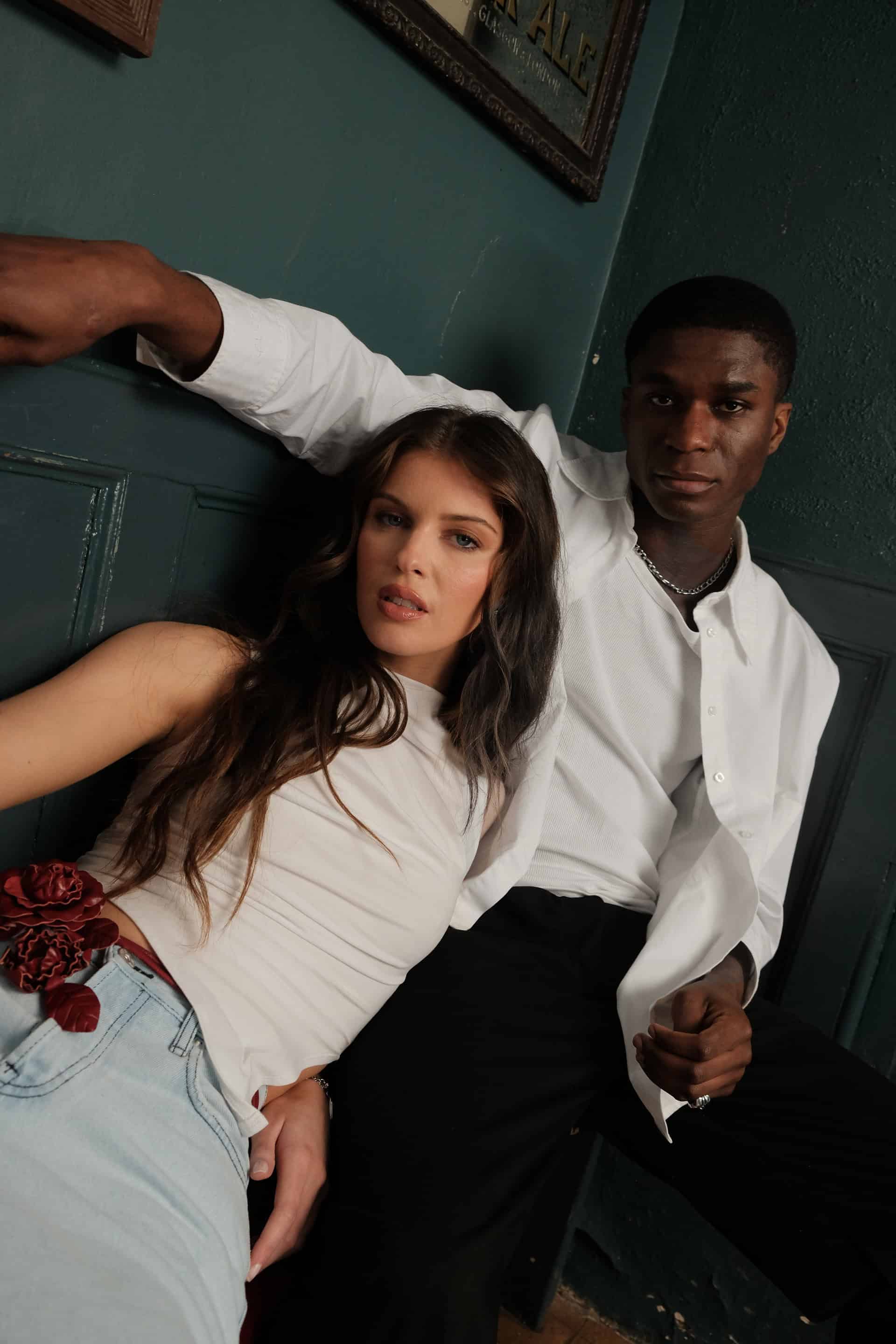Models Emma and Patrick sitting casually in the corner of a bar, looking directly into the camera alluringly, wearing staple pieces of The Sixth Language's debut collection "The Intro Collection"
